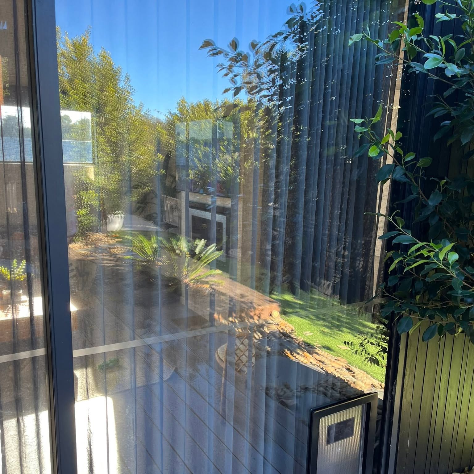 A pet door fitted into a large fixed glass panel looking onto a sunny garden and decking