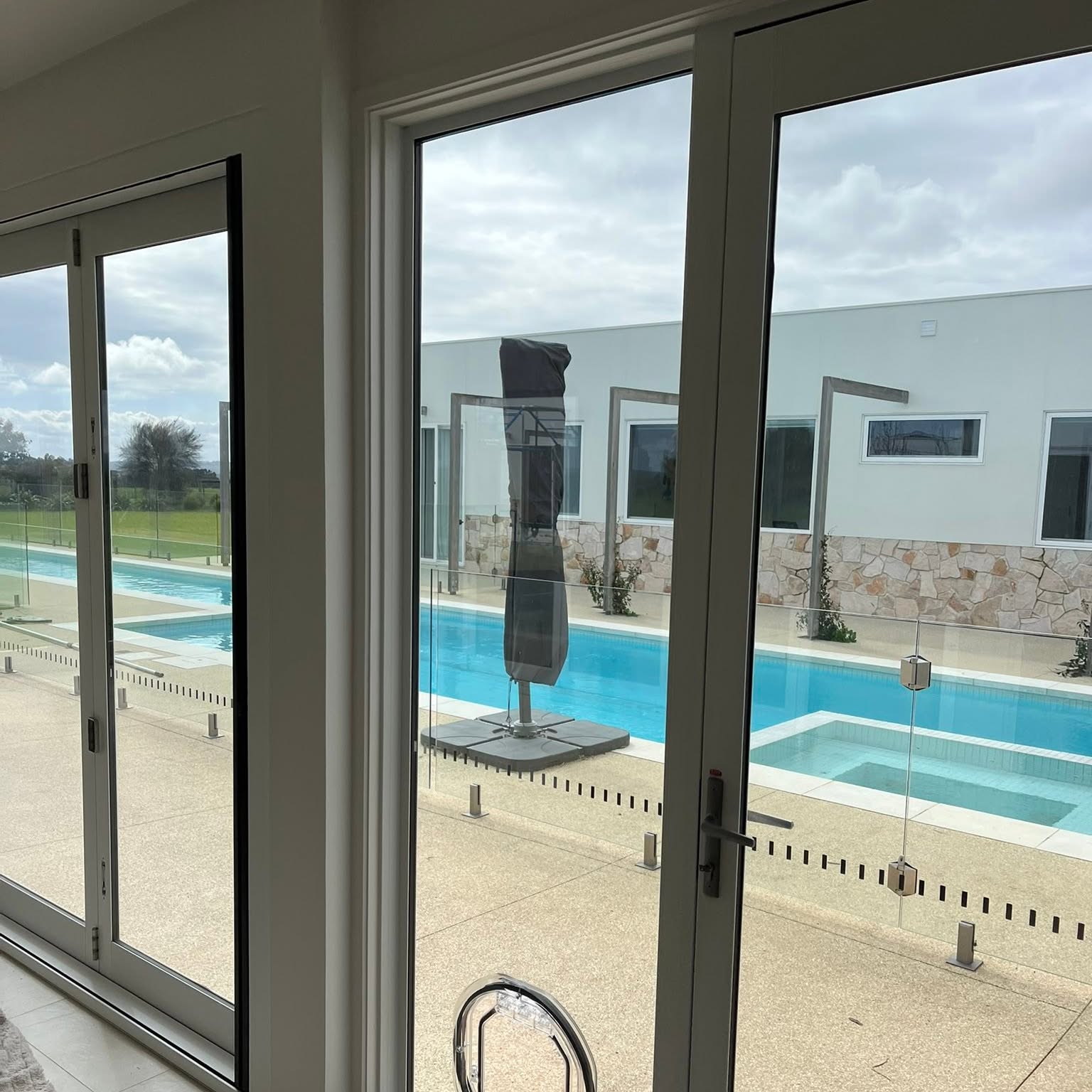 A pet door fitted into the lower pane of bifold doors, looking out across a swimming pool with frameless glass pool fencing