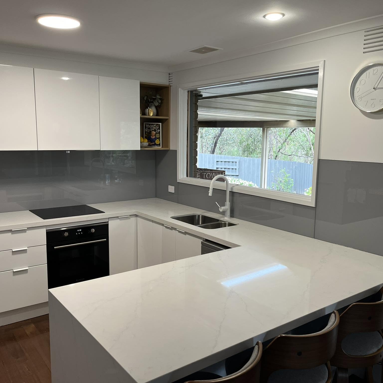 A grey toughened glass splashback fitted behind a white kitchen benchtop and cooktop