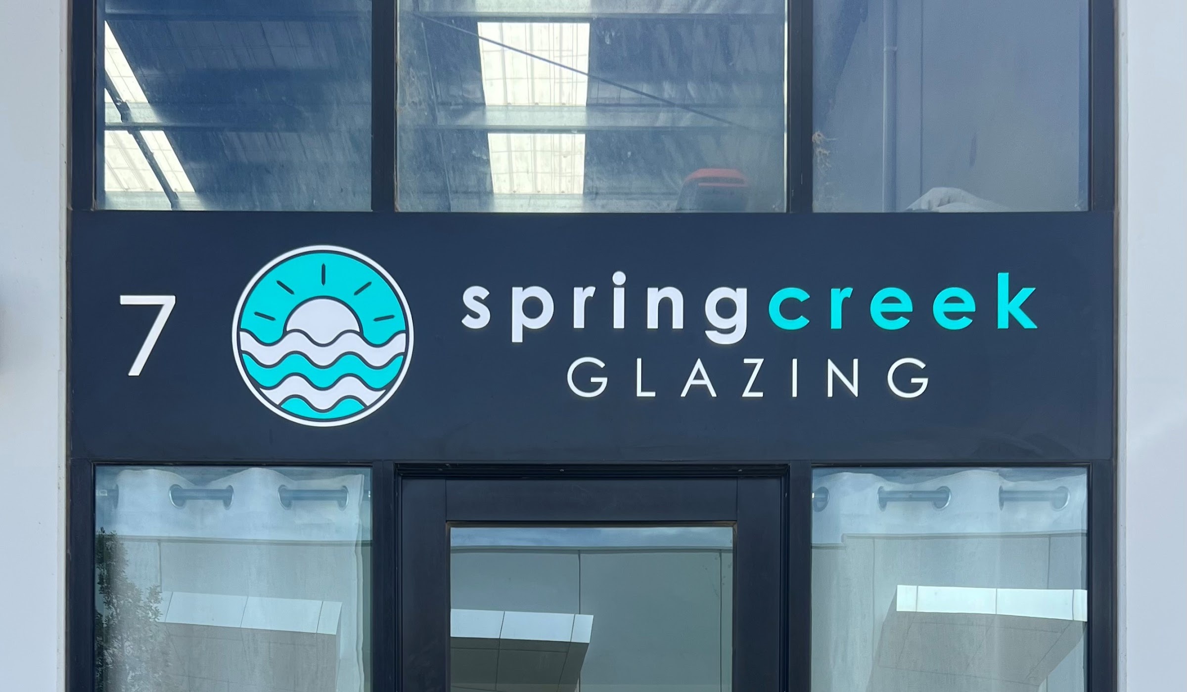 The Spring Creek Glazing shopfront sign, a navy fascia with the teal sun and waves logo, at unit 7 Cylinders Drive Torquay