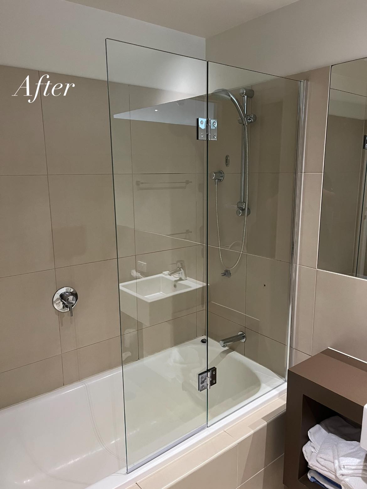 A frameless glass shower screen fitted over the same bath after the work
