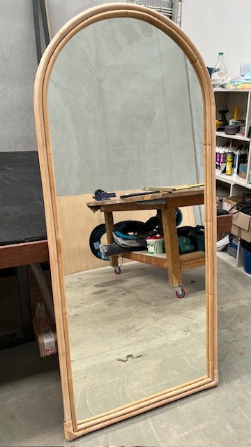 A tall arched mirror with a rattan frame standing on the workshop floor